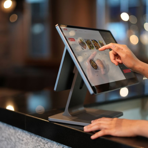 Close-up of a hand interacting with a touchscreen POS system in a restaurant setting.